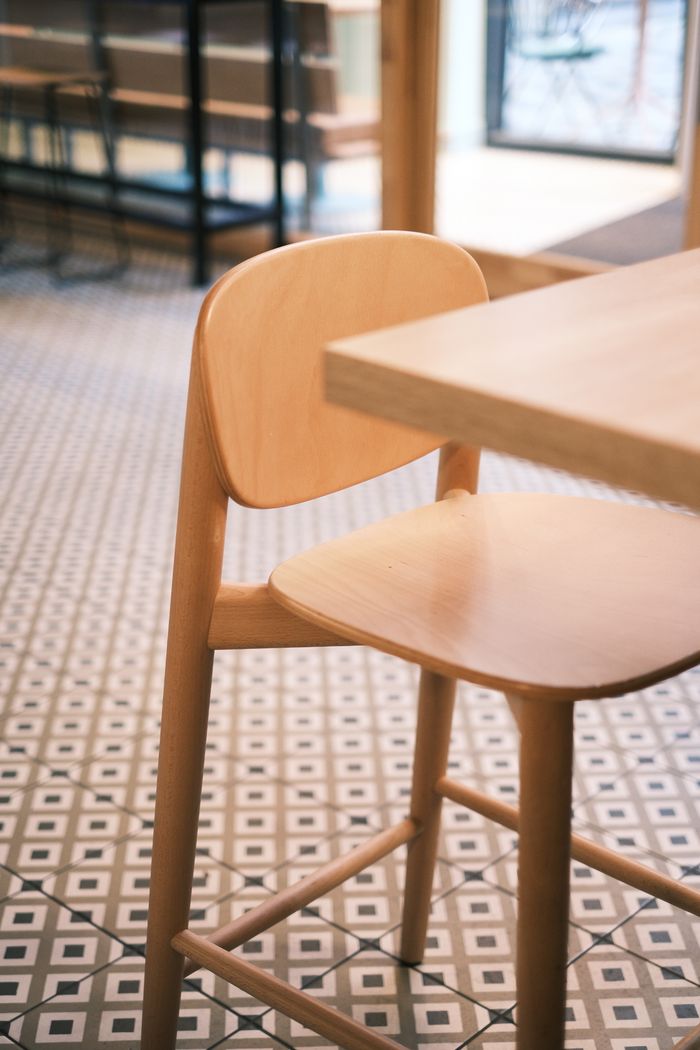 Stylish wooden chair in a contemporary cafe setting with geometric floor tiles.