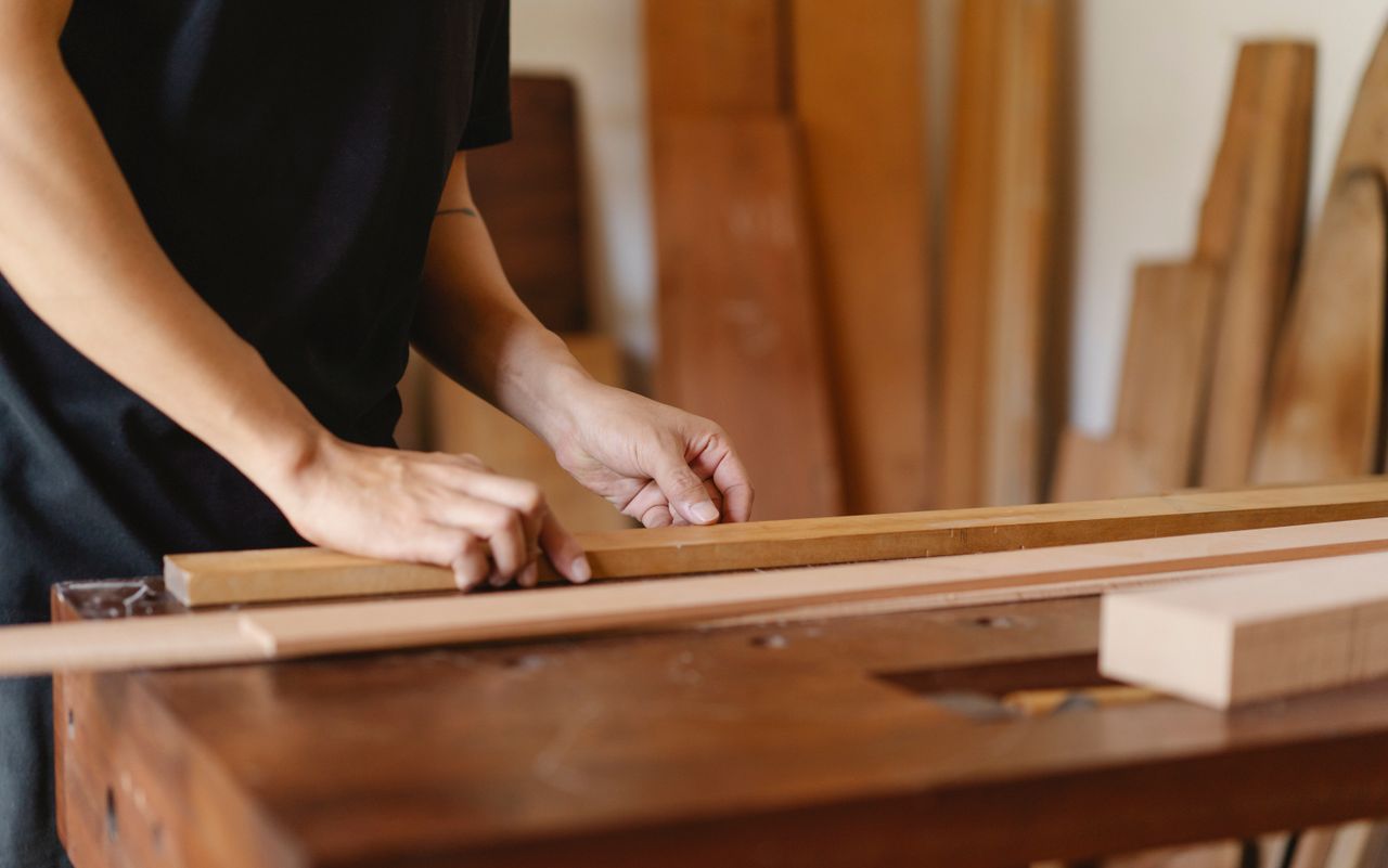 Crop anonymous male doing carpentry with timber plank on table on blurred background of workshop
