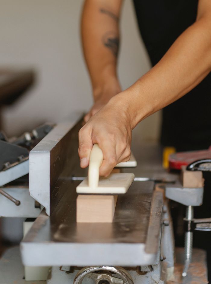 Crop anonymous male carpenter with manual instruments flatting wooden plank on professional equipment in workshop
